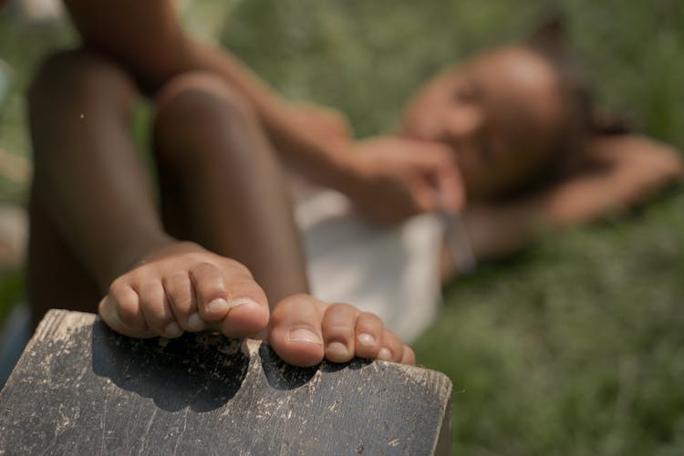 Legs Of Teenage Girl Laying Bare Foot On Back With Hand Under Head In Park