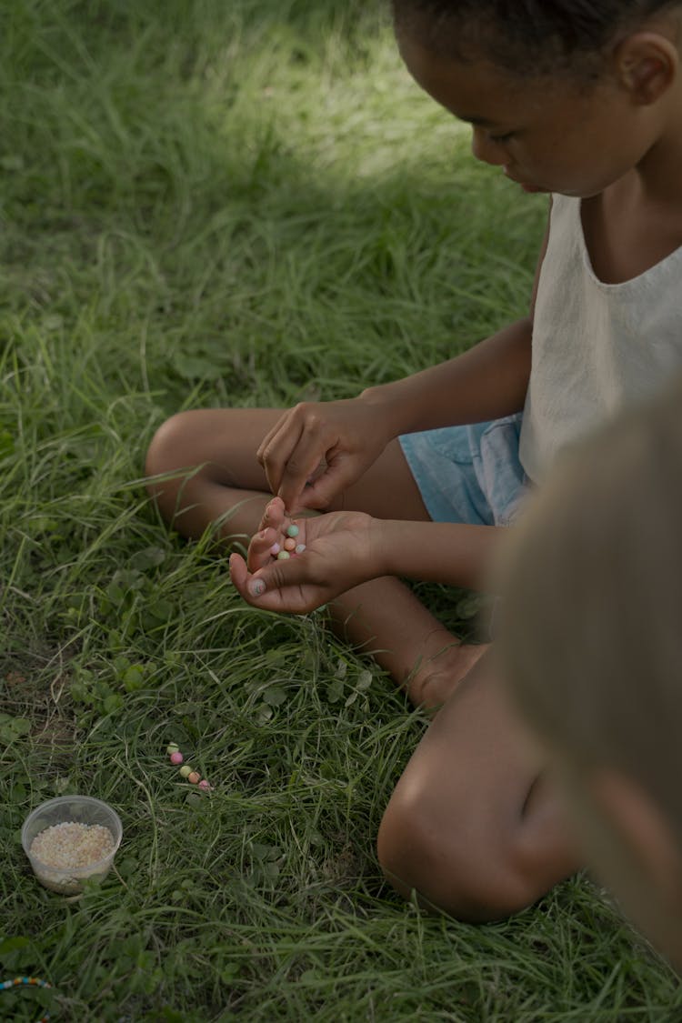 Girls Sitting On Grass Making Beads Bracelets