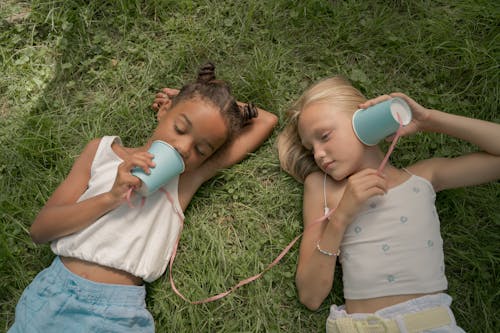 Free Two Teenage Girls Laying on Grass and Playing Telephone Call Using Paper Cups on String Stock Photo