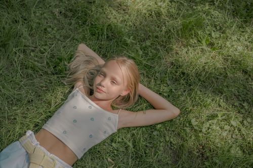 Free Teenage girl lying on grass with hands behind head enjoying the summer sun. Stock Photo