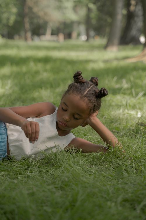 Free A young girl with Afro-American hair relaxes on the grass in a summer park, enjoying a peaceful moment. Stock Photo