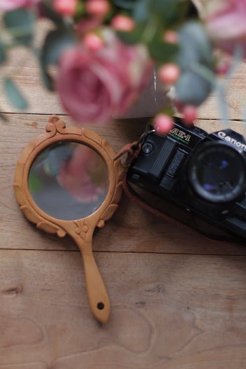 Black Canon Camera Beside a Mirror on Wooden Surface