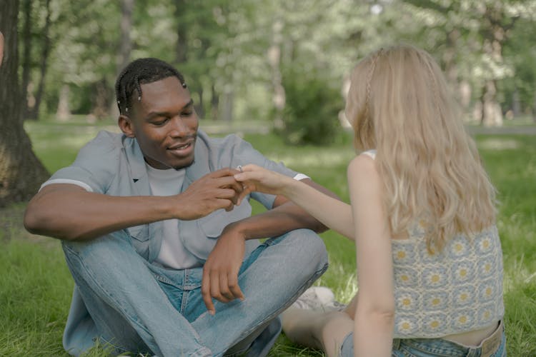 Couple Sitting On The Grass And Man Looking At The Ring On The Female Finger