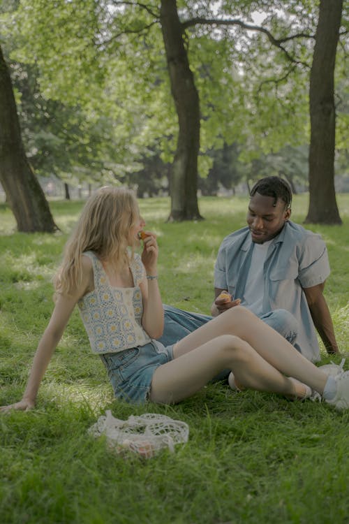 Young Couple Sitting on Lawn in Park and Having Meal