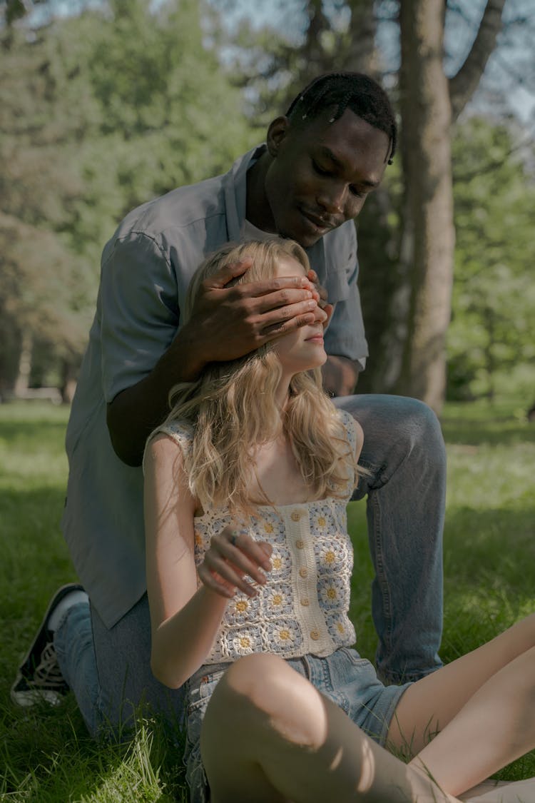 Young Man Kneeling Behind His Sitting Girlfriend And Covering Her Eyes With Hands