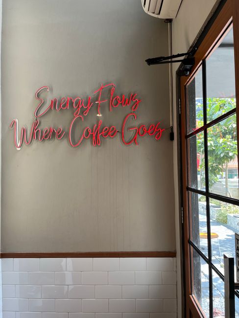 Stylish cafe interior featuring a neon sign with the quote 'Energy Flows Where Coffee Goes'.