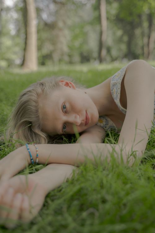 Free A young blonde woman laying on the grass in a sunlit park. Stock Photo