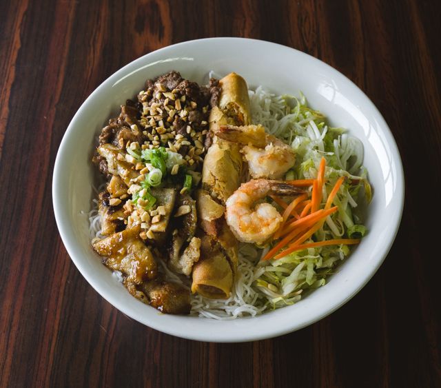 Close-up of a flavorful Vietnamese vermicelli bowl featuring grilled meats, shrimp, and vegetables.