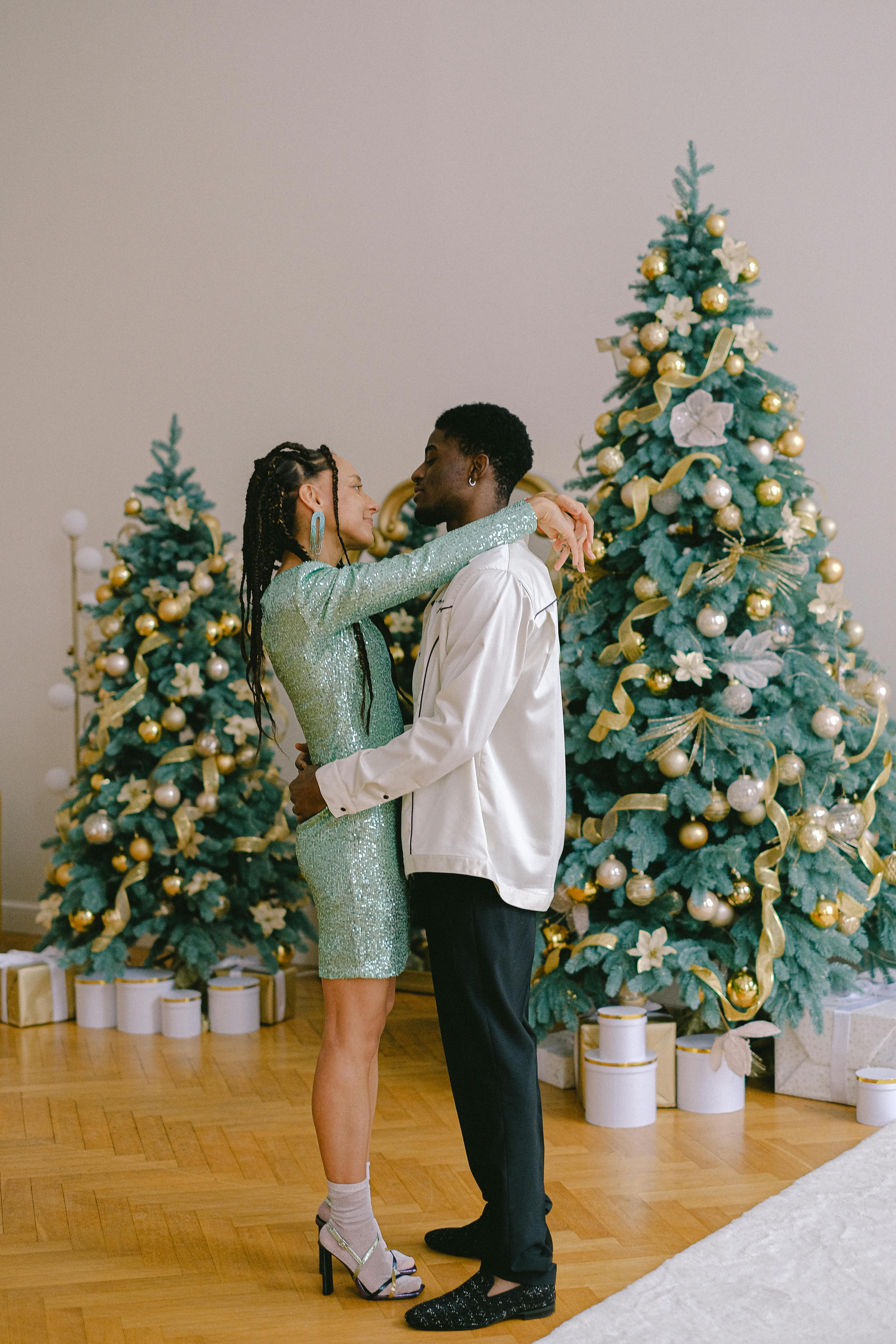 A couple shares a romantic moment in front of festive Christmas trees indoors.