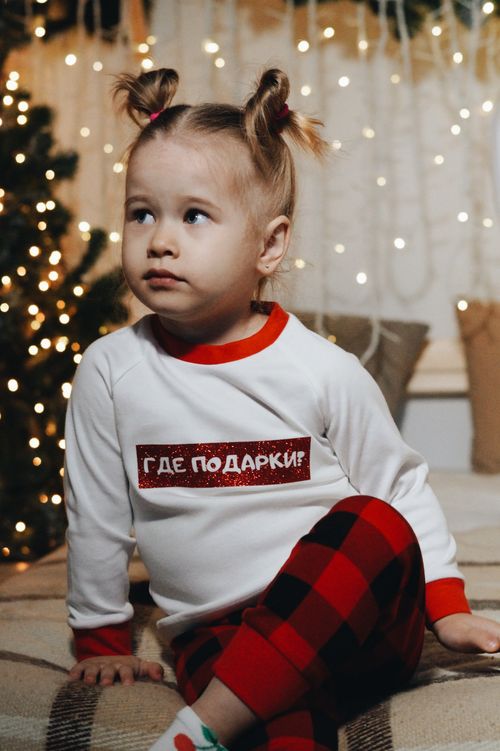 Free Cute child sits indoors wearing festive pajamas with holiday lights in the background. Stock Photo