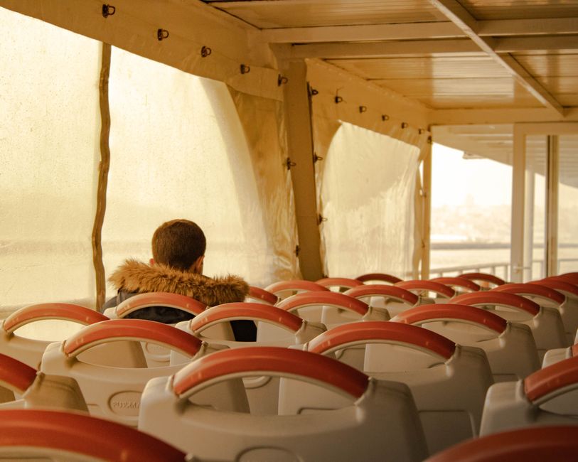 A person sits alone on a boat surrounded by empty seats on a calm day.