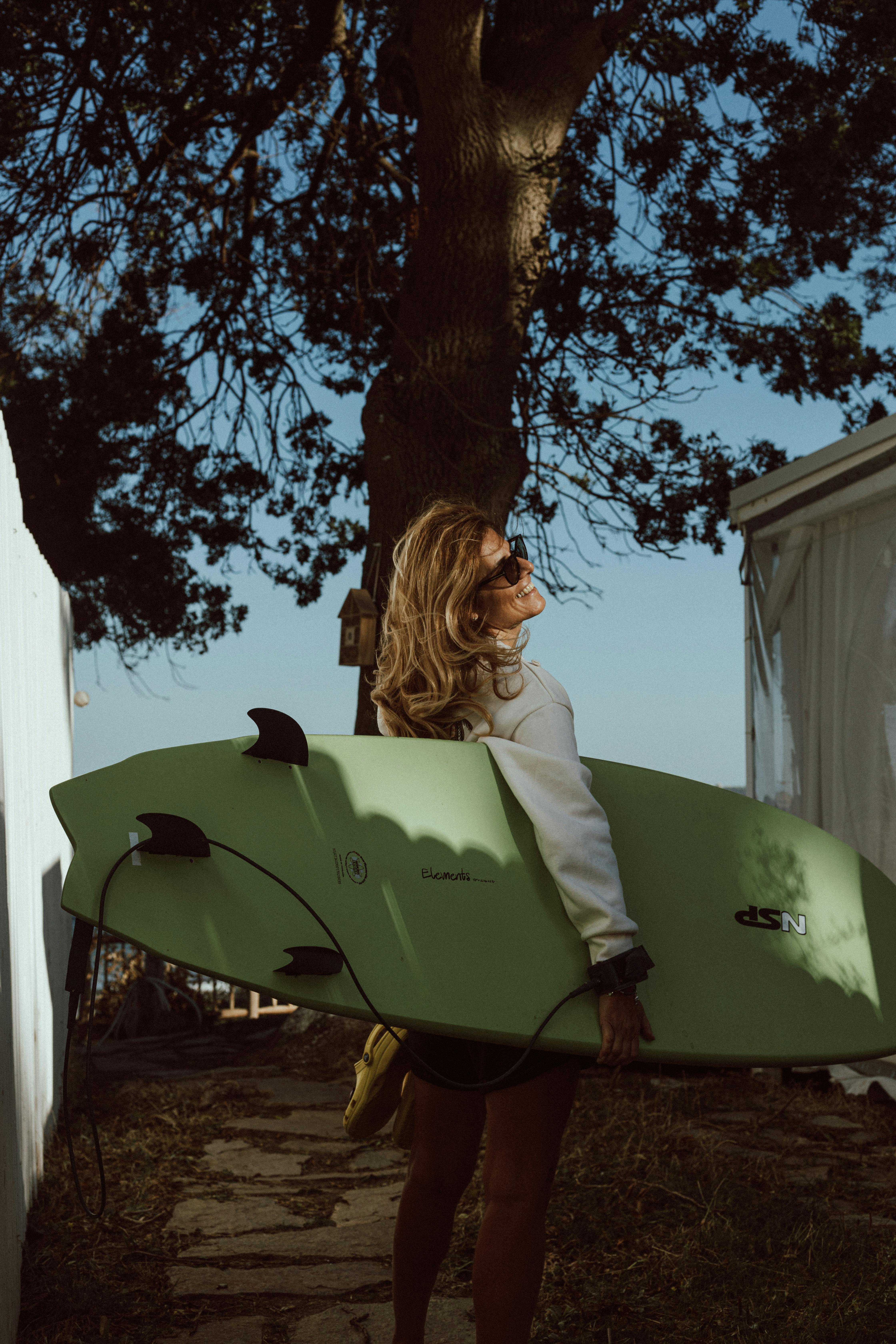 Woman carrying a surfboard outdoors, enjoying sunny day.