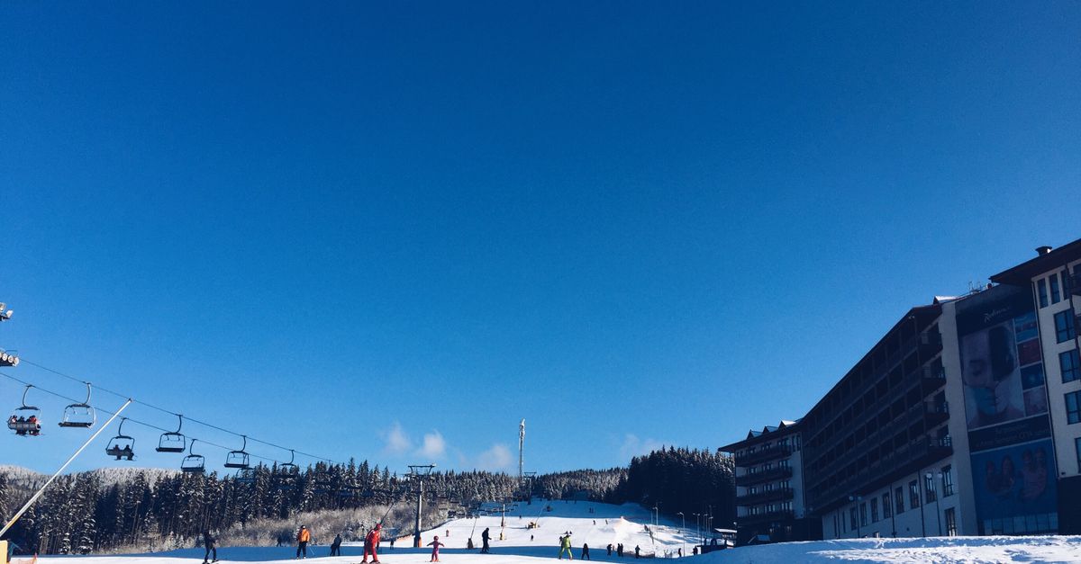 Skiers on a snowy slope with a lift and a hotel.