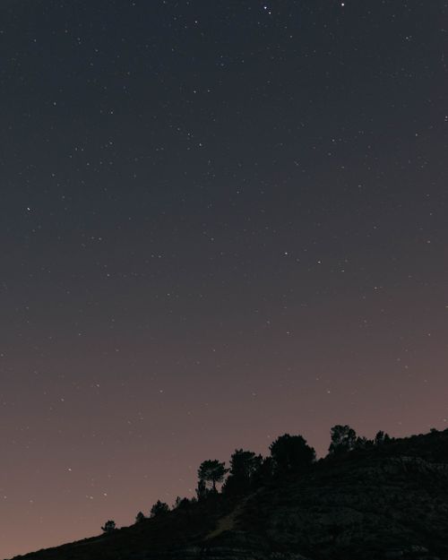 Free A serene night sky filled with stars over a silhouetted hilltop, capturing the peaceful essence of the evening. Stock Photo