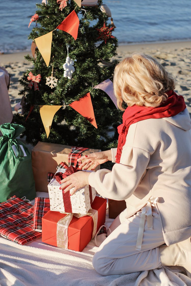 Back View Of A Woman Arranging Presents Near A Christmas Tree At The Beach