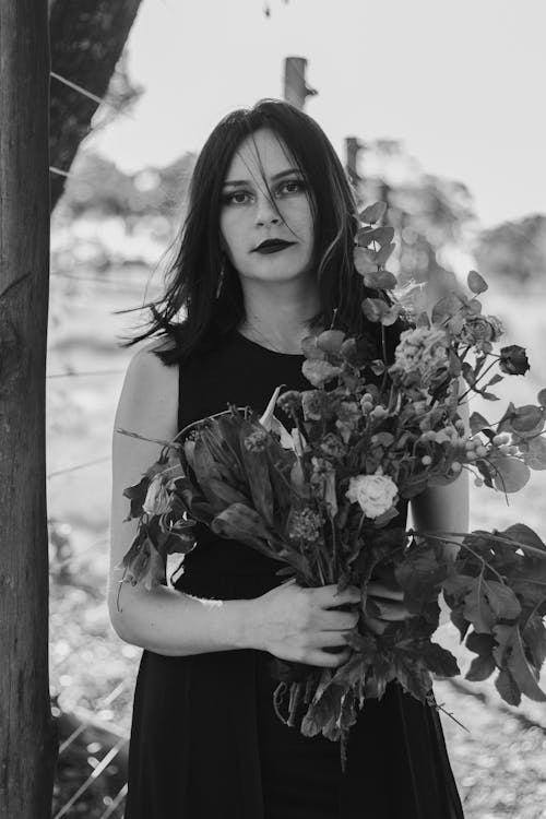 Grayscale Photo of a Woman Holding Dry Flowers