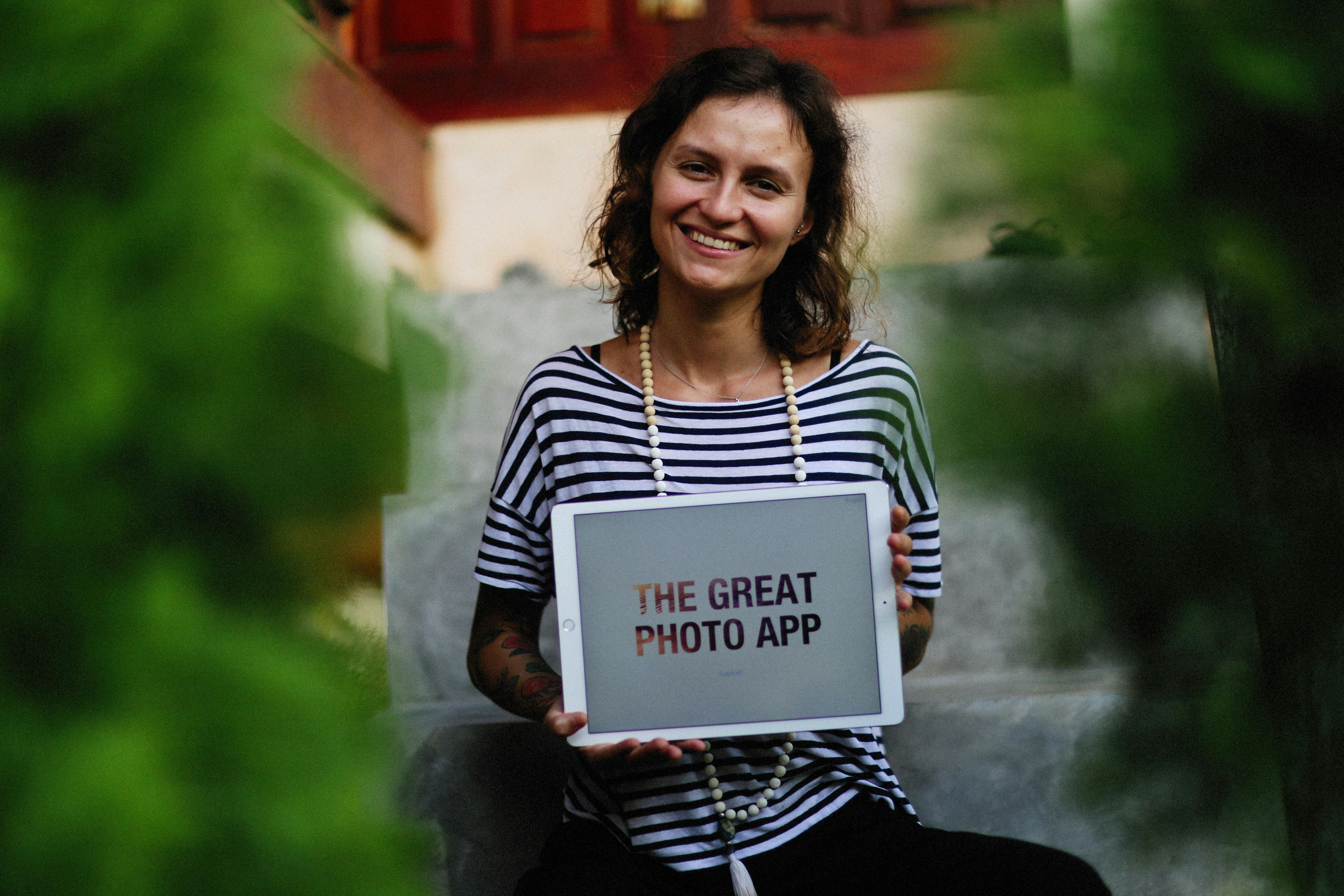 Woman sitting on steps holding tablet with displayed app. Outdoor setting.