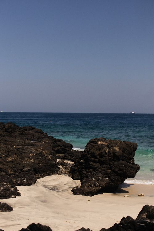 Free Peaceful beach scene with rocks, sand, and a vast blue sea under clear sky. Stock Photo