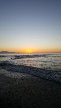 Beautiful sunset over a serene beach with gentle waves and a clear sky.