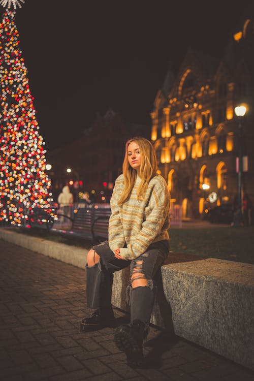 Woman in Brown and Gray Jacket Sitting on Sidewalk during Night Time