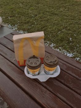 McDonald's takeaway coffee cups and paper bag on a wooden bench outdoors in Kyiv park. — photo by Ya Demenina