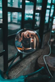 Artistic shot capturing a photographer's reflection in a round side mirror indoors.