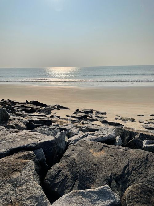 Free Calm beach scene with rocks, sand, and the shimmering sea under a daylight sky. Stock Photo