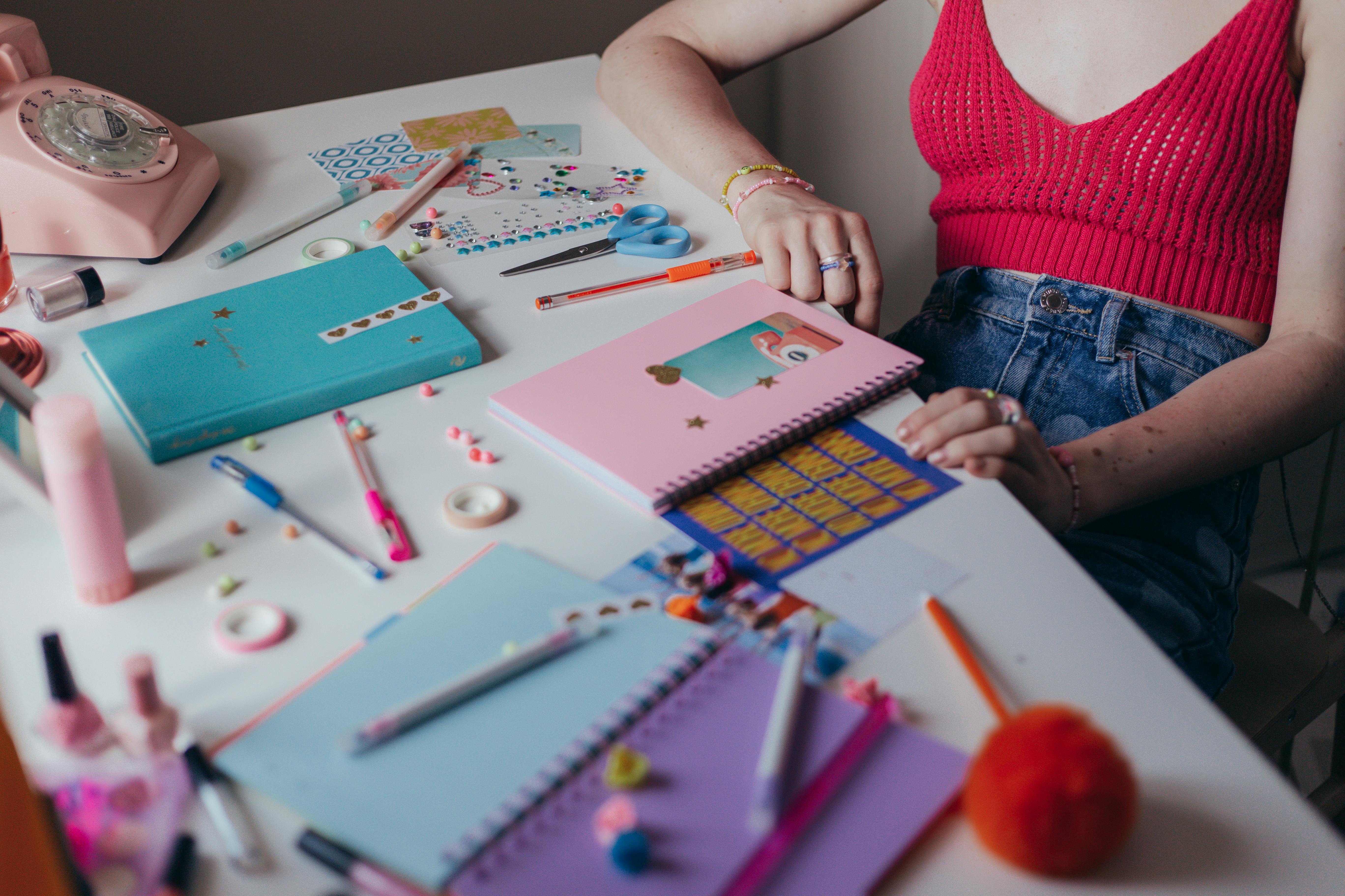 girl sitting at a desk full of colorful notebooks pens and stickers