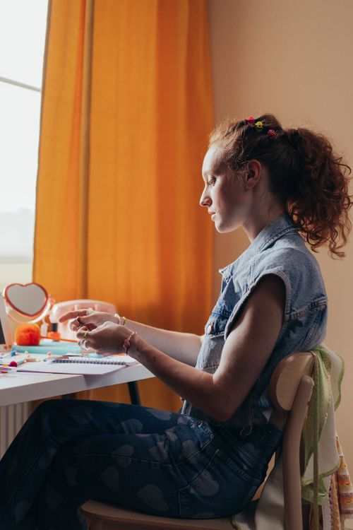Free Teen girl creating art at a desk, surrounded by colorful craft supplies in a serene room. Stock Photo