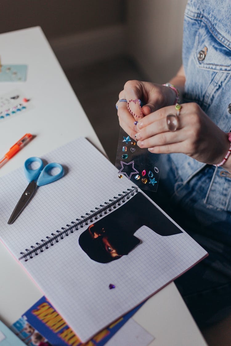 Close-up Of Girl Putting Paper Cutouts And Stickers In A Notebook 