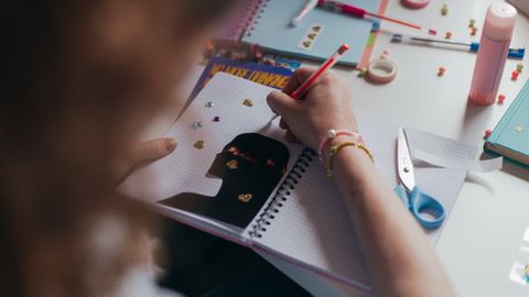 A student decorates a notebook with stickers and colorful supplies, engaging in a creative art project.