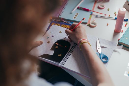 A student decorates a notebook with stickers and colorful supplies, engaging in a creative art project.