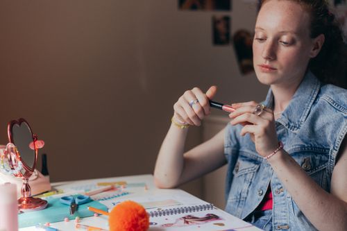 Free Young woman applying makeup at desk with cosmetic products, creating a beauty routine. Stock Photo