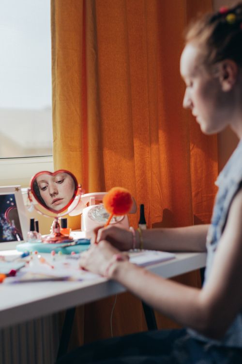 Free A young woman writes at a desk with accessories, reflected in a heart-shaped mirror. Stock Photo