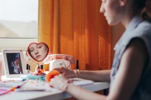 Free A woman sits at a vanity, her reflection visible in a heart-shaped mirror next to a vintage telephone. Stock Photo