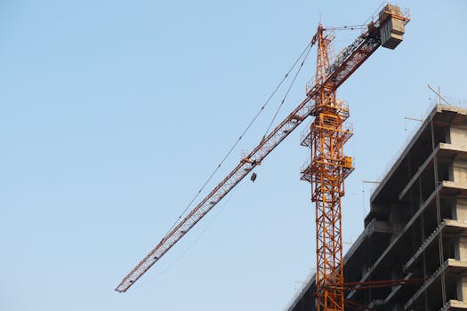 Low angle view of a tower crane beside a building under construction against a blue sky.