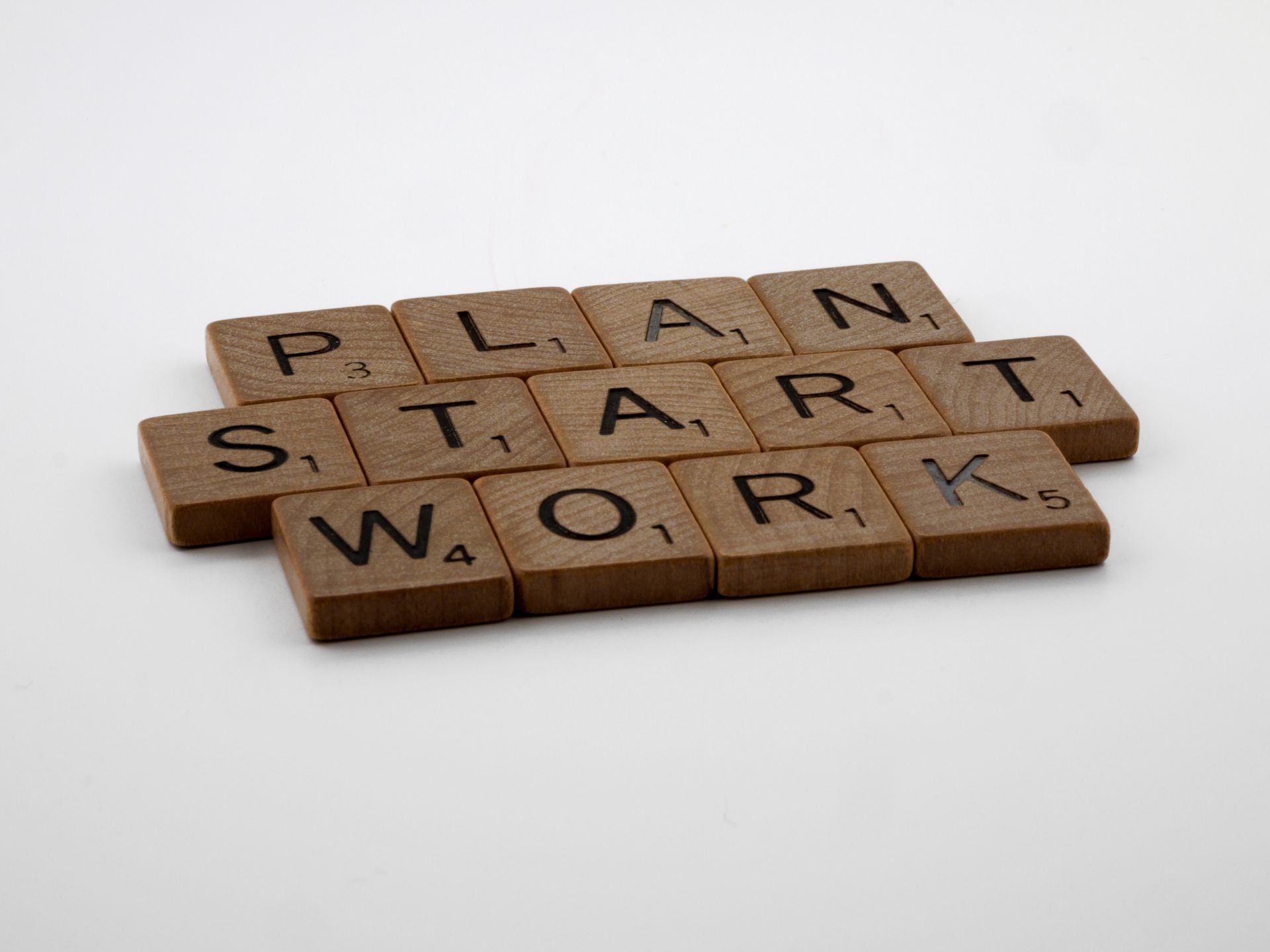 Scrabble tiles arranged to spell Plan Start Work on a white surface, symbolizing motivation.