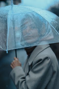 A woman under a transparent umbrella captures the mood of a rainy day outdoors.