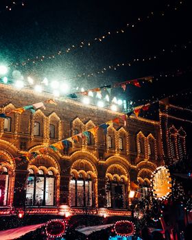 A beautifully lit historic building in Moscow during a festive evening celebration, adorned with colorful lights.