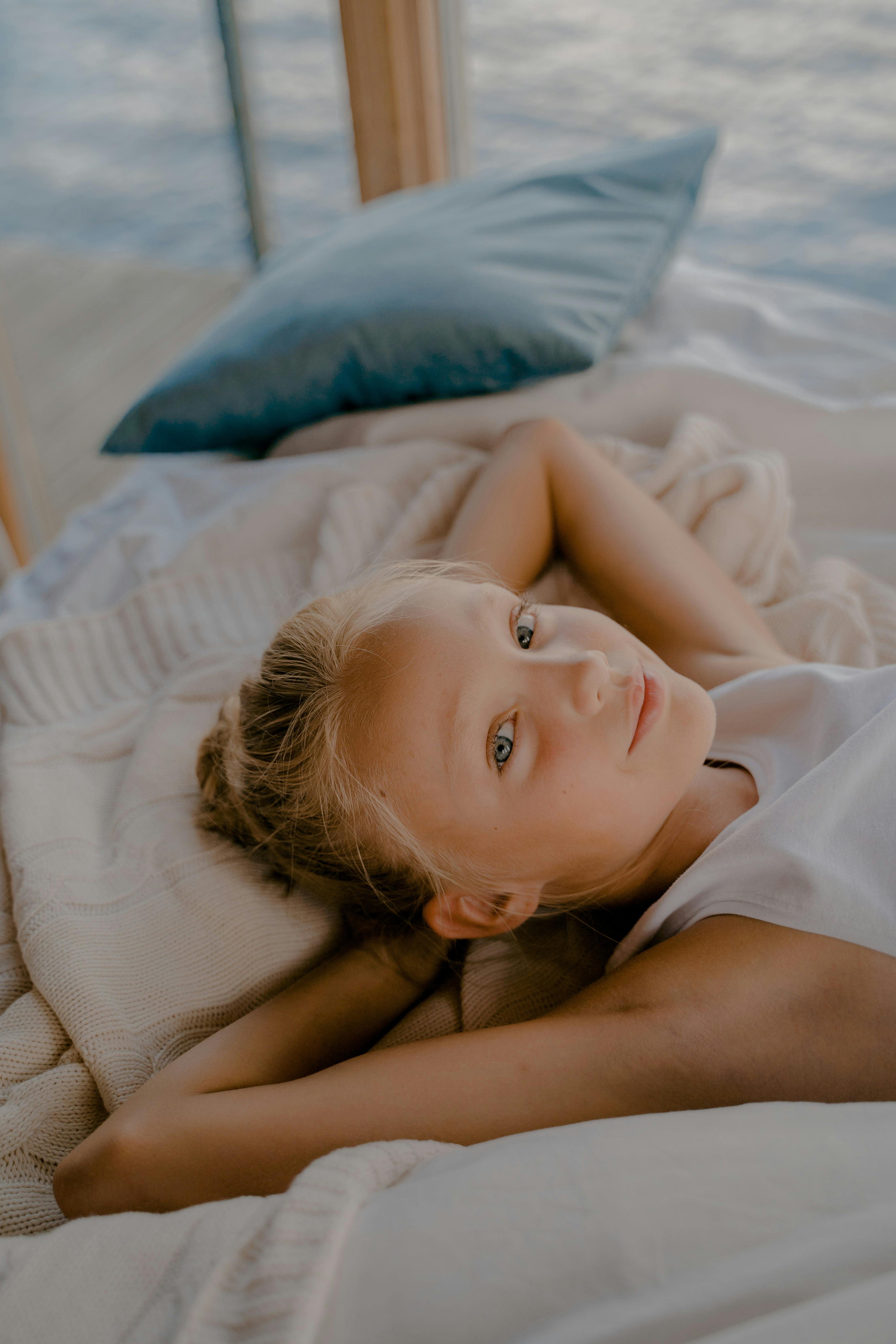 Young girl lying on a bed with hands behind head, enjoying a serene moment indoors.