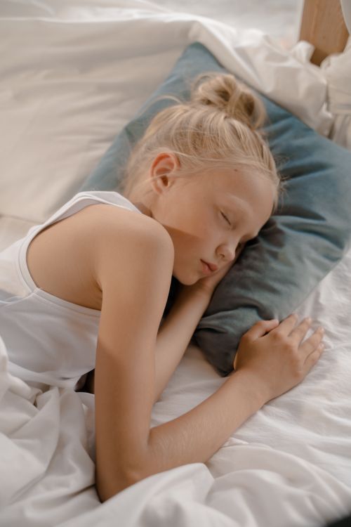 Free A serene image of a young girl sleeping peacefully on a soft bed with a blue pillow. Stock Photo