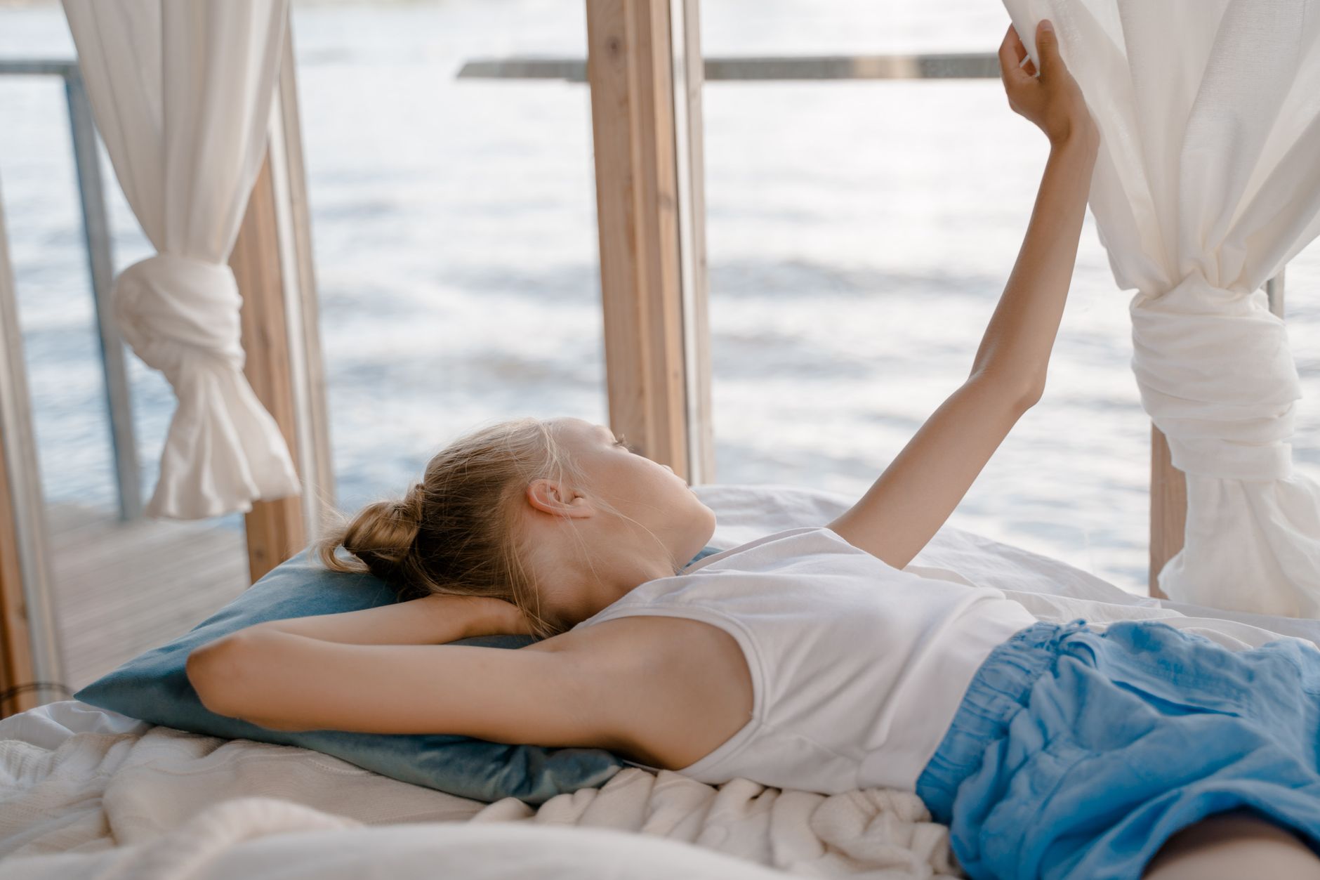 A young girl lies back and enjoys a peaceful view by the waterside window.