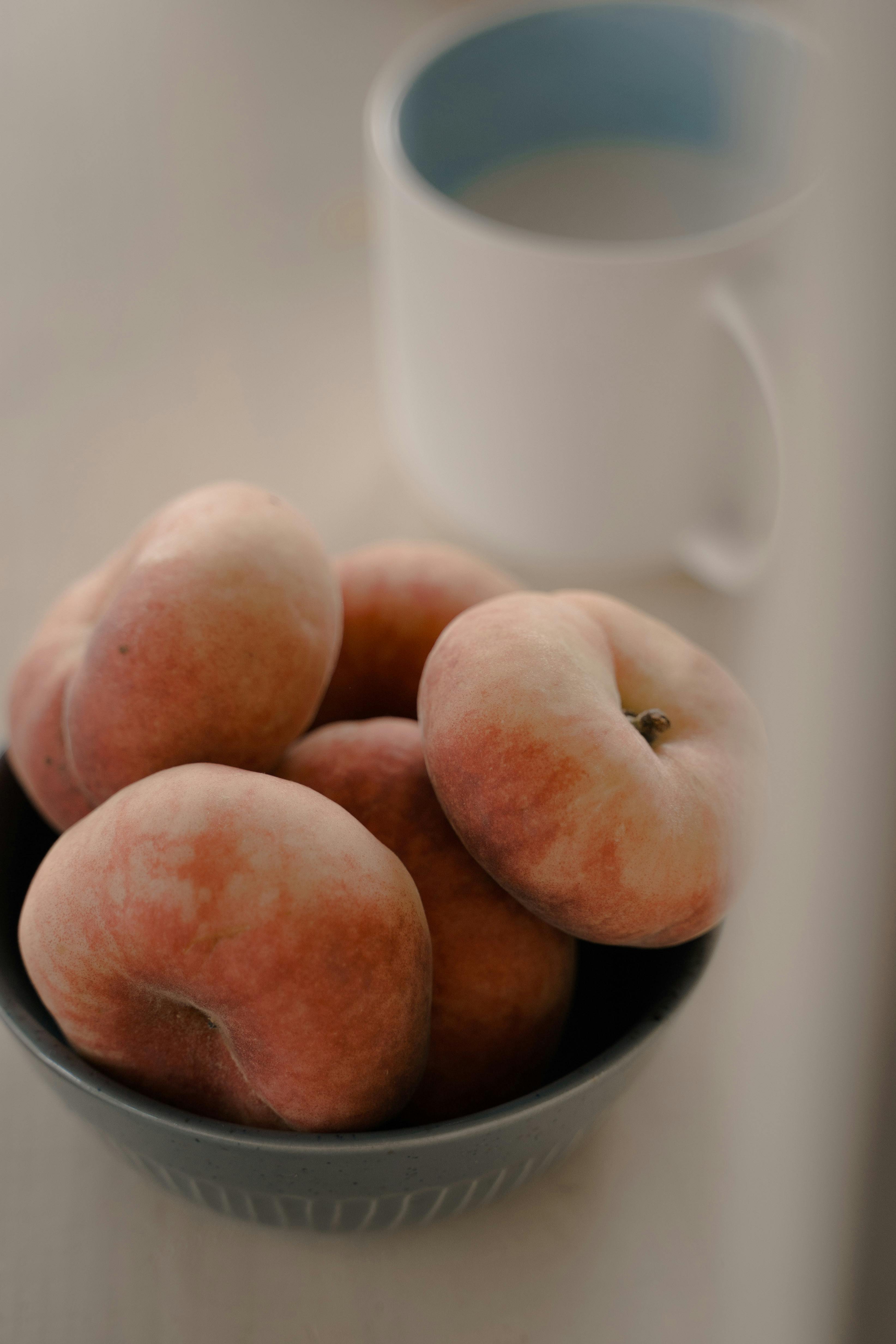 Close-up of juicy peaches piled in a bowl with a mug, evoking freshness and simplicity.