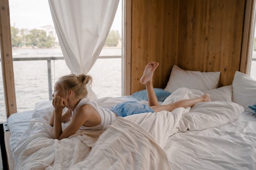 Free Blond Girl Lying on Bed and Looking through Window Stock Photo