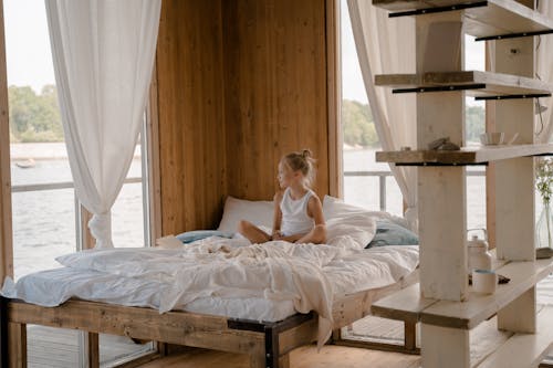 Free Girl Sitting on Bed and Looking Through Window at Sea  Stock Photo