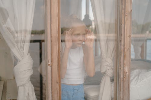 Free Sad Child Looking through Window Stock Photo