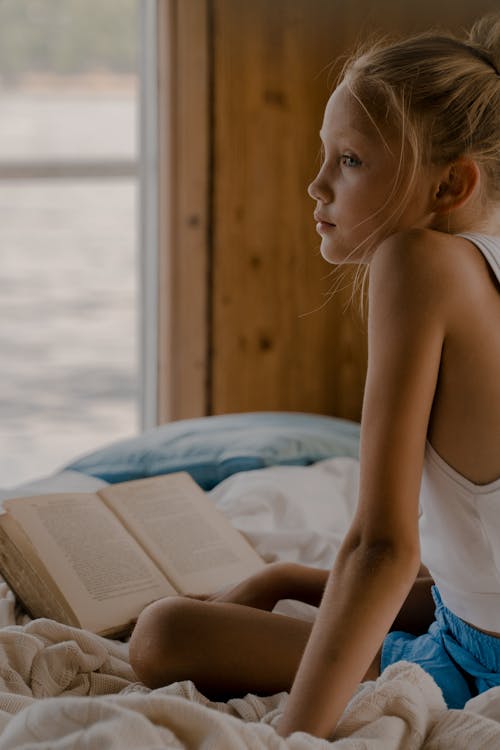 Sad Child Sitting on Bed with Book