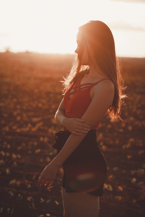 Free A woman poses gracefully in a field during sunset, creating a striking silhouette against the golden light. Stock Photo