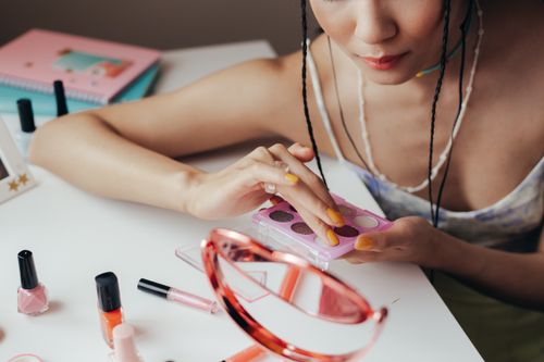 Free Woman using eyeshadow palette with cosmetics scattered on a table, reflecting in mirror. Stock Photo