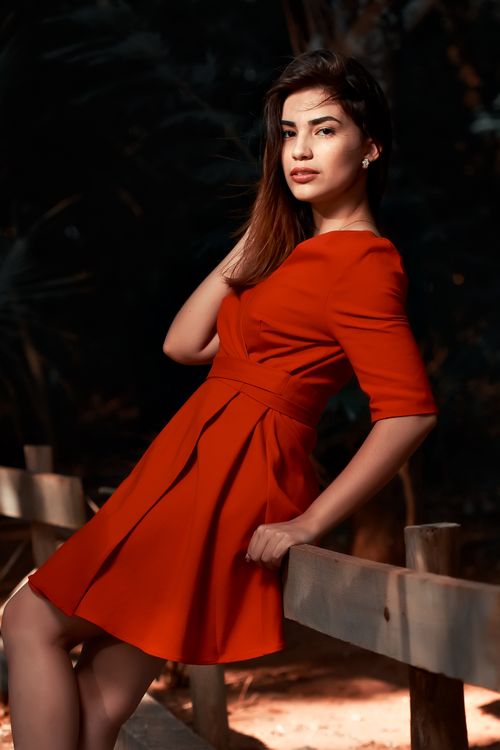 Free A stylish woman in a vibrant red dress poses gracefully by a wooden fence. Stock Photo